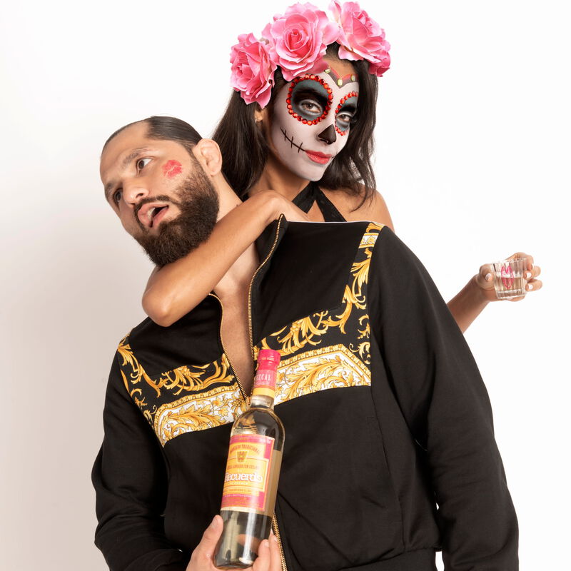 Jorge Masvidal holds a bottle of Recuerdo Mezcal while a woman dressed as Catrina jokingly holds him in a headlock.